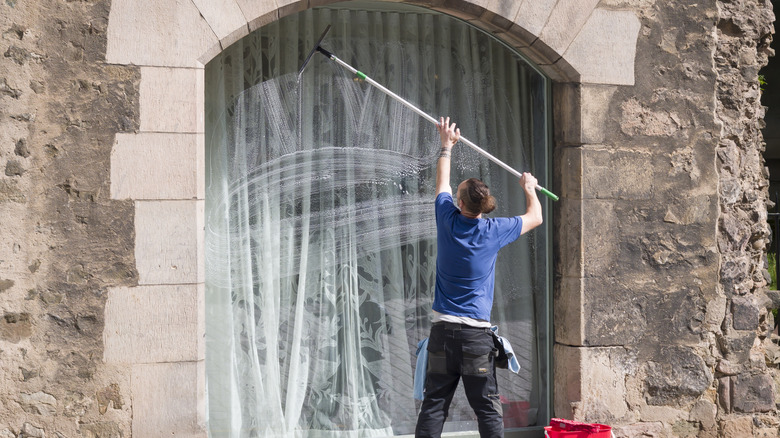 A man uses a window cleaning tool to reach a high window