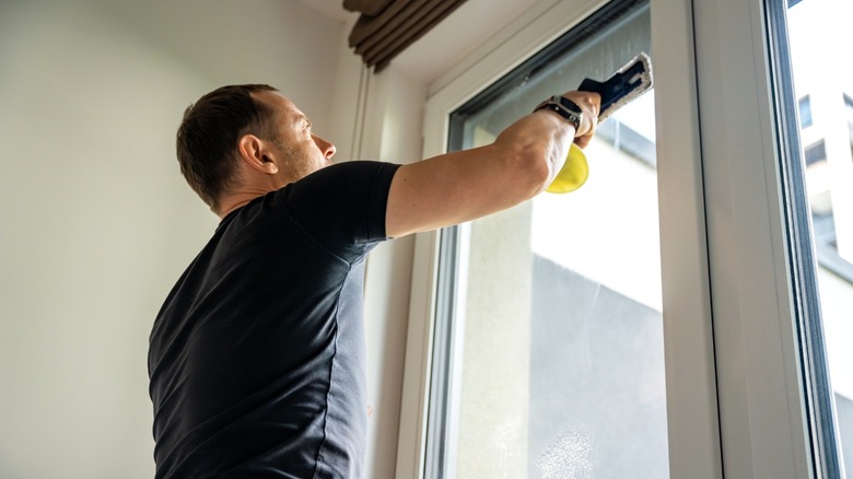 A man cleaning high interior window with microfiber pad