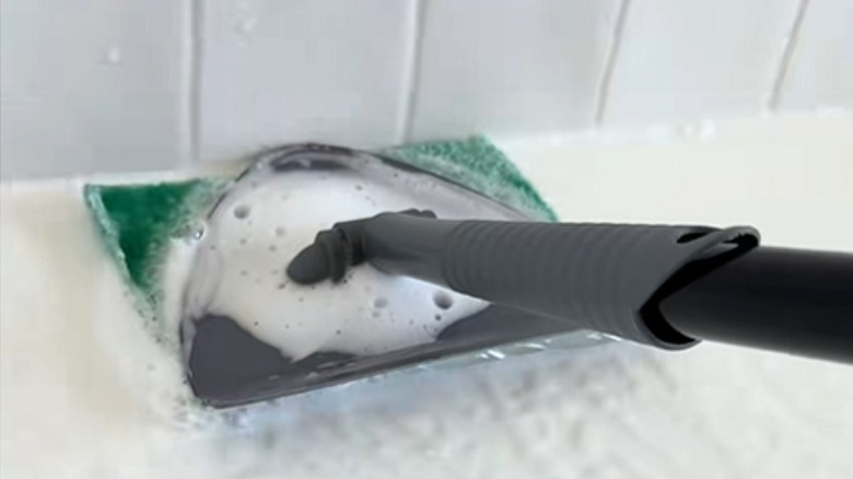 A triangular mop head fitted with a scrubbing pad and handle scour dirty shower tiles.
