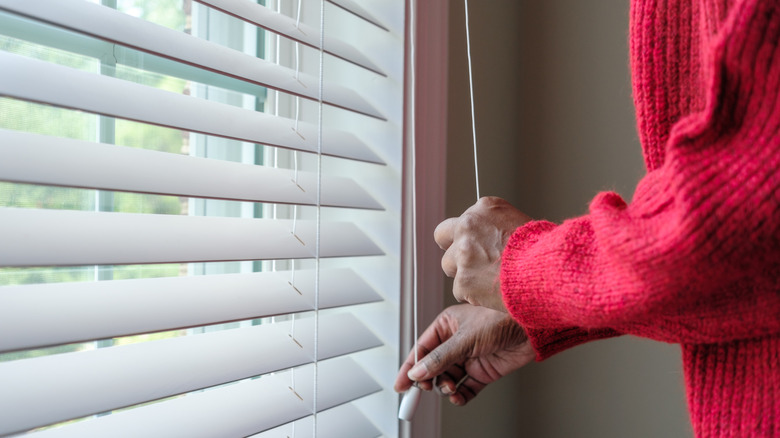 A person using the pull cord to open the blinds.