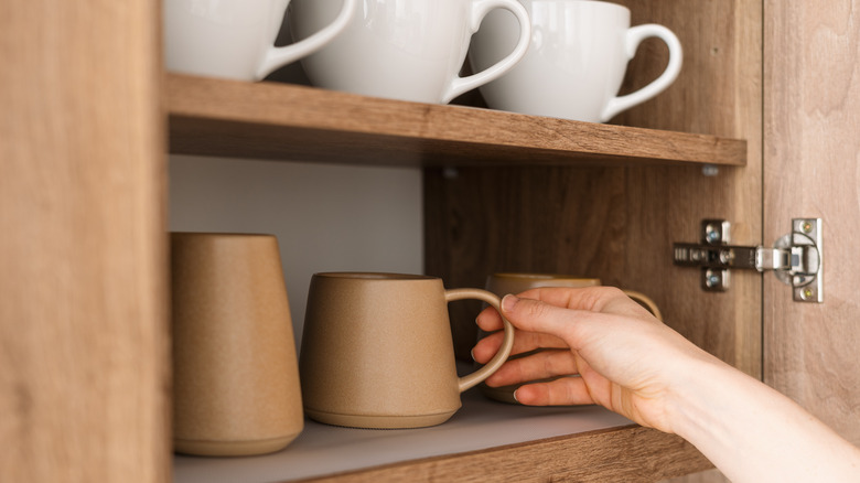 Hand reaches for mug in cupboard full of mugs