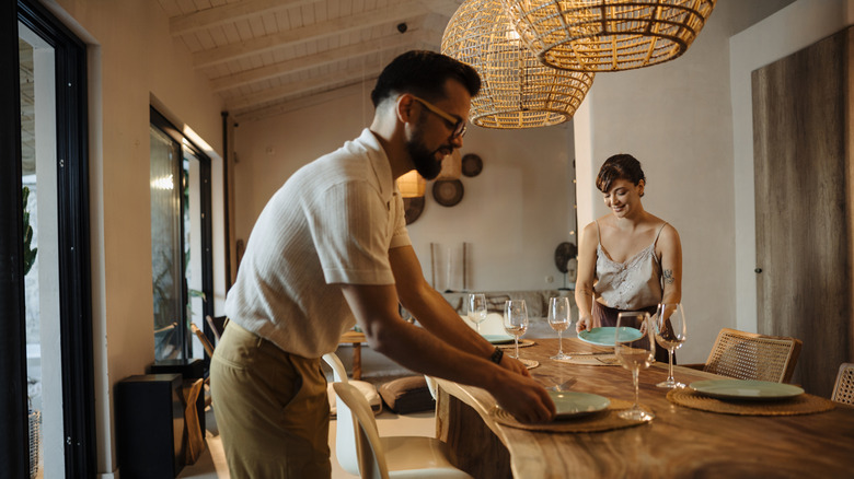 A young interracial couple sets a dinner table.