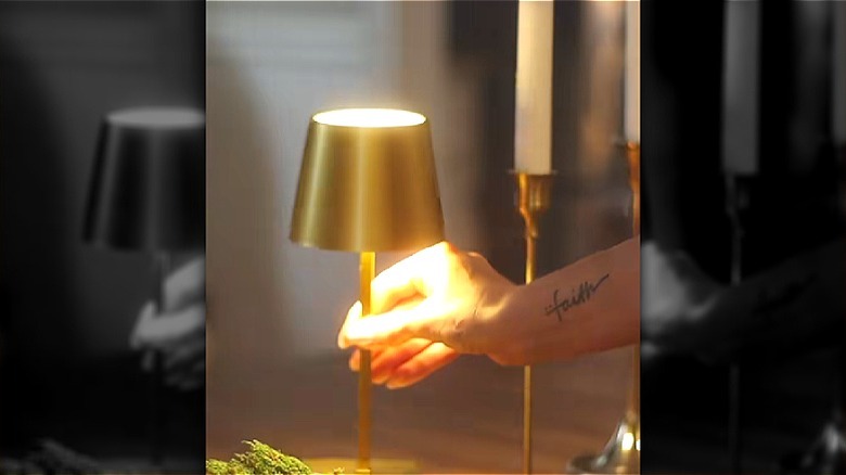 Hand placing a gold Dollar Tree touch lamp on a dinner table