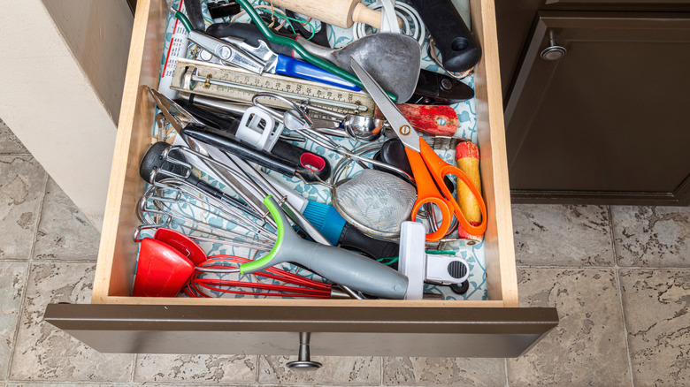 A messy kitchen drawer with scissors and other random items