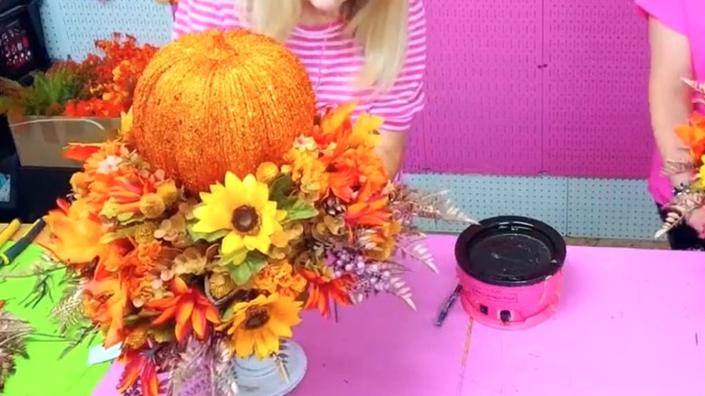 Woman in pink shirt stands behind a glittery pumpkin and floral centerpiece