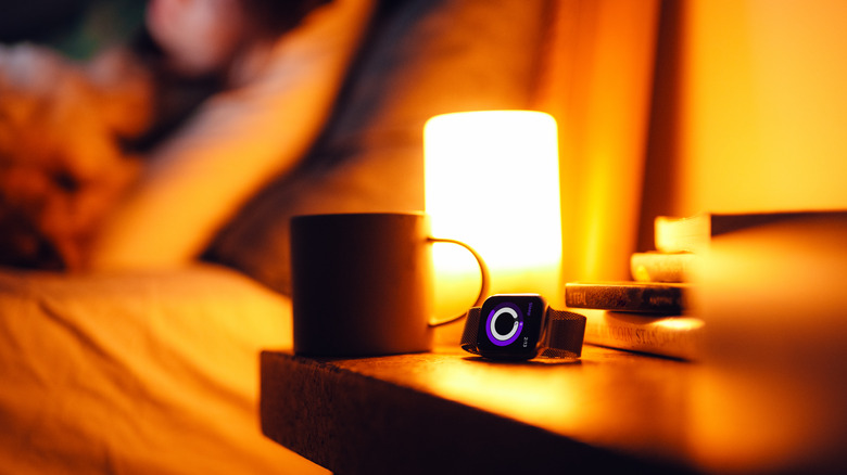 A nightstand with a mug, watch, books, and light