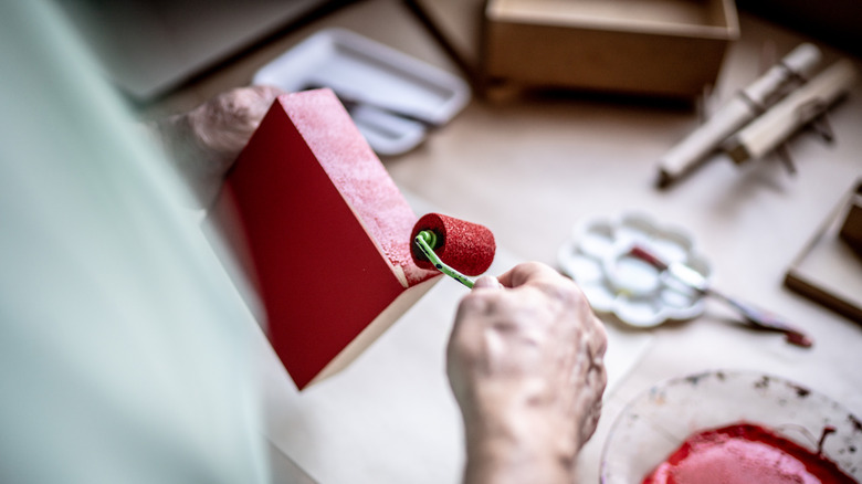 A person paints a piece of wood red with a roller brush.