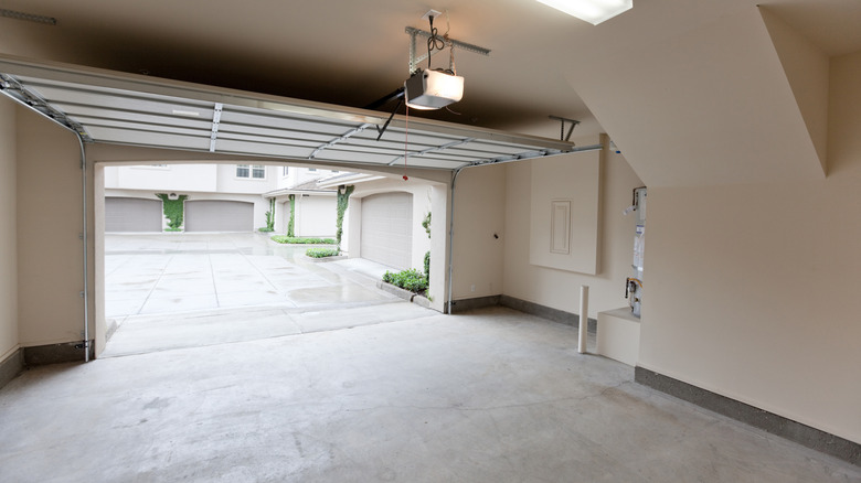 An empty two-car garage with open door, with a view looking from inside out towards the street, shows an idyllic street somewhere in suburban America.