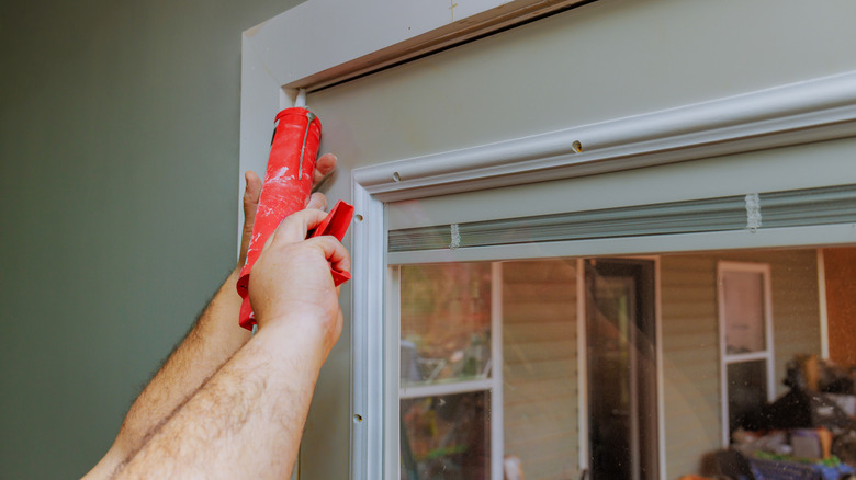 Carpenter using caulk gun to seal gaps around door frame in home improvement effort.