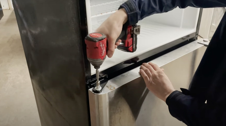 Person unscrewing a refrigerator door at the top hinge