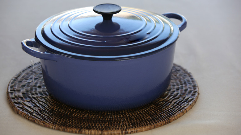 An up close look at a blue casserole dish sitting on a wicker potholder on a gray surface