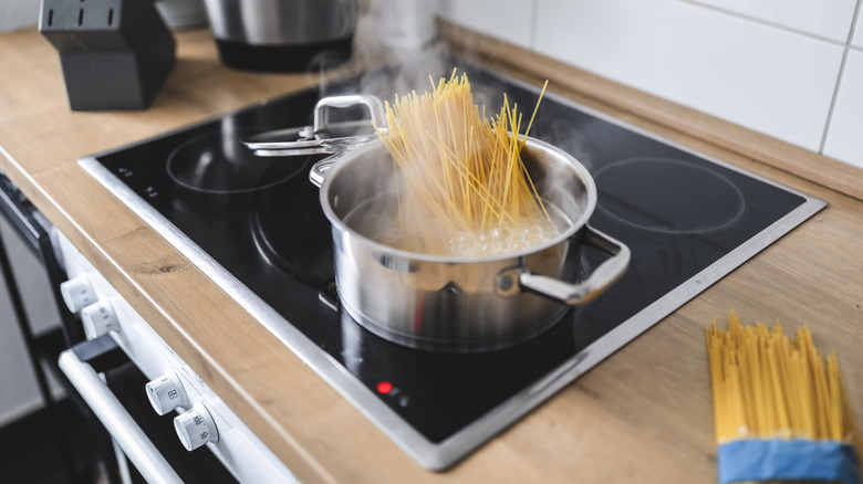 Spaghetti is boiling in a stainless steel pot on an electric stovetop.