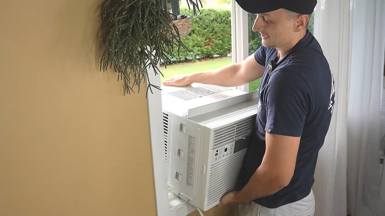 Man lifting a window air conditioner into an open window