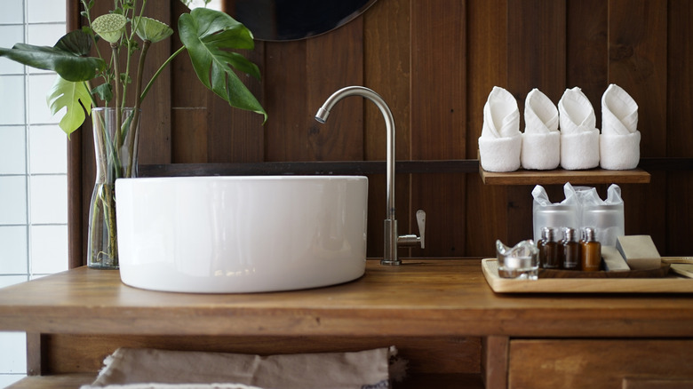 White bathroom sink on wooden vanity with folded towels and toiletries