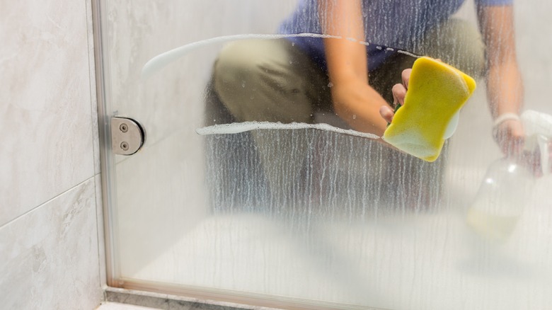 Someone cleaning a glass shower door covered in water spots and soap scum.