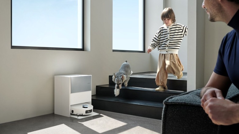 Child and dog walking down stairs in front of robot vacuum at its dock