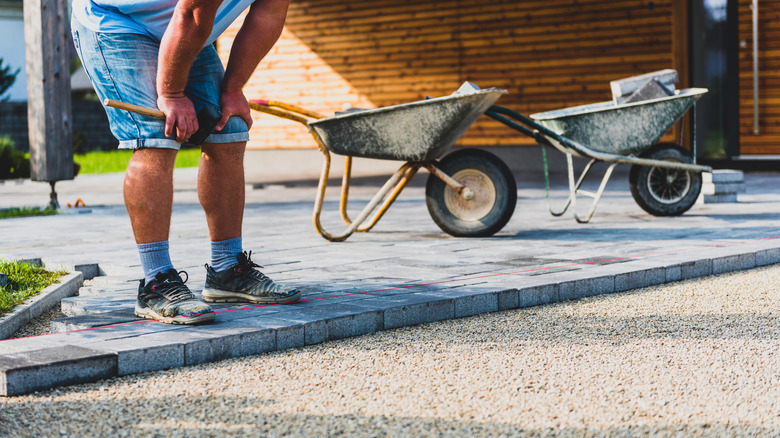 A man's legs in shorts working on a driveway with two wheelbarrows behind him.