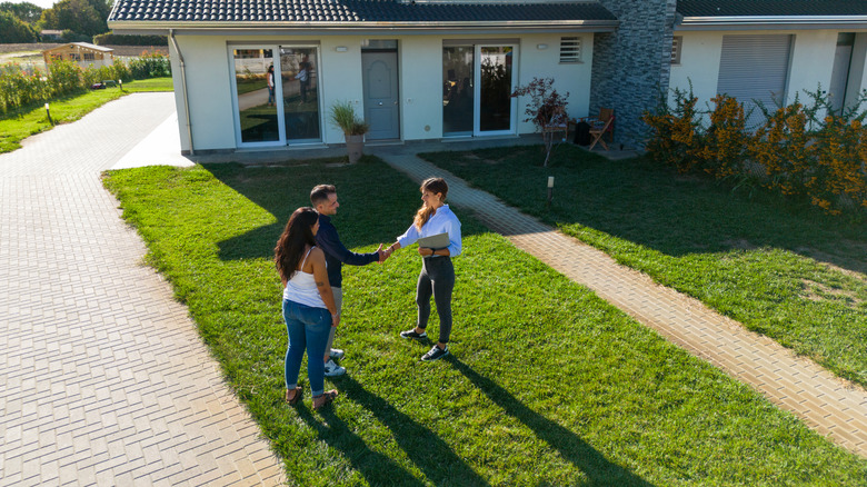A real estate agent shakes hands with buyers in a home's front yard