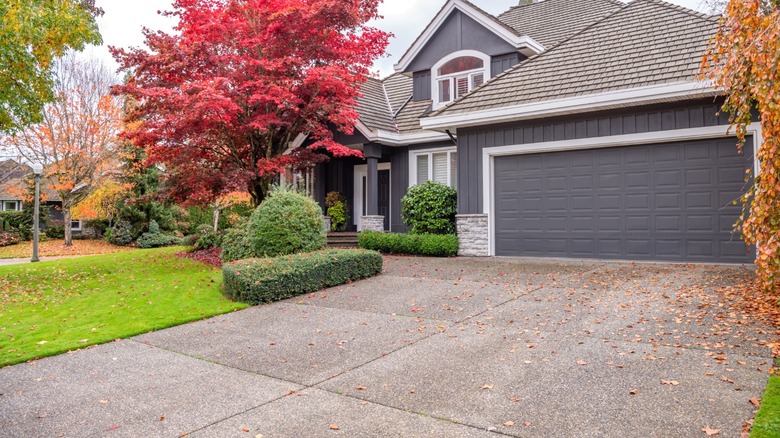 Front of a gray suburban house with a lawn and a driveway in fall