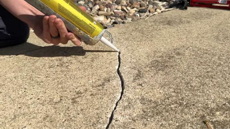 A person mending concrete driveway crack with concrete sealant