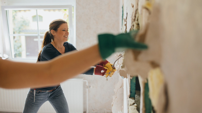 Two women demolish an interior wall