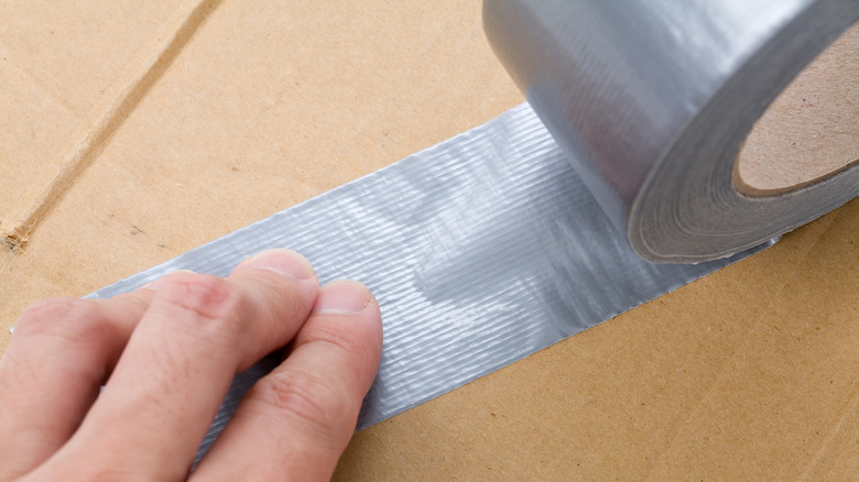 Hand pressing duct tape on cardboard