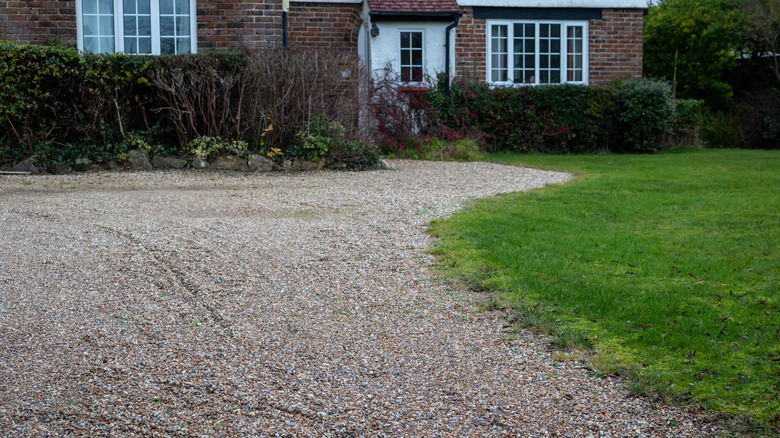 A gravel driveway with grass growing into it around the edge