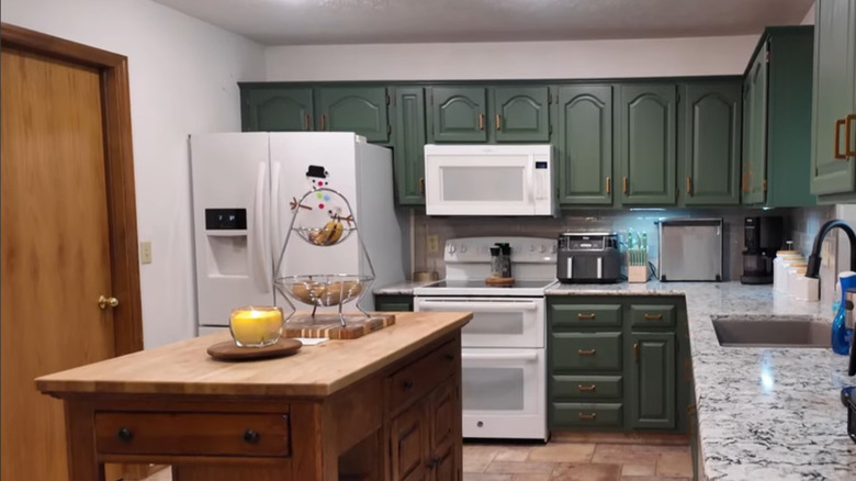A modern kitchen with green cabinets and honey oak accents.