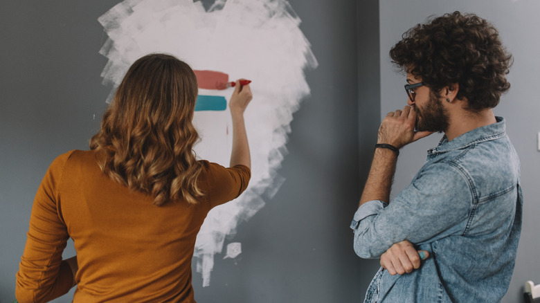 A man and woman standing in front of paint color options on wall.
