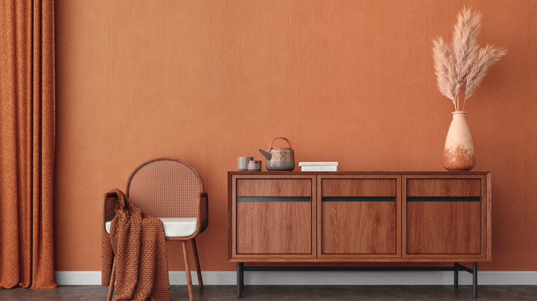 A rusty orange wall in a room with brown furniture and orange curtains.
