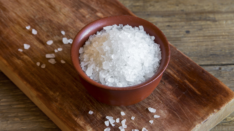 A small red-brown bowl of coarse sea salt sitting on a wooden plank