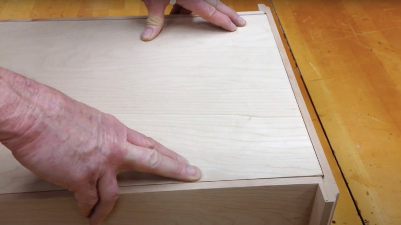 A person constructing a drawer made with rabbet joints fits the bottom piece of wood into place