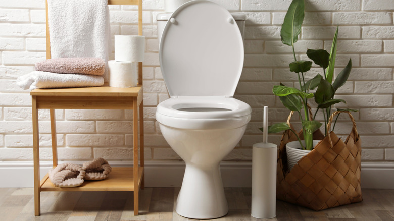A toilet bowl with various daily-use items placed on a wooden chair beside it