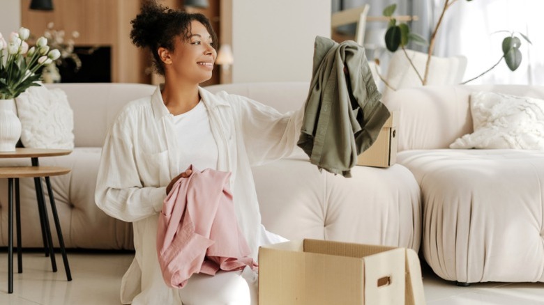 Smiling woman decluttering clothes in her living room