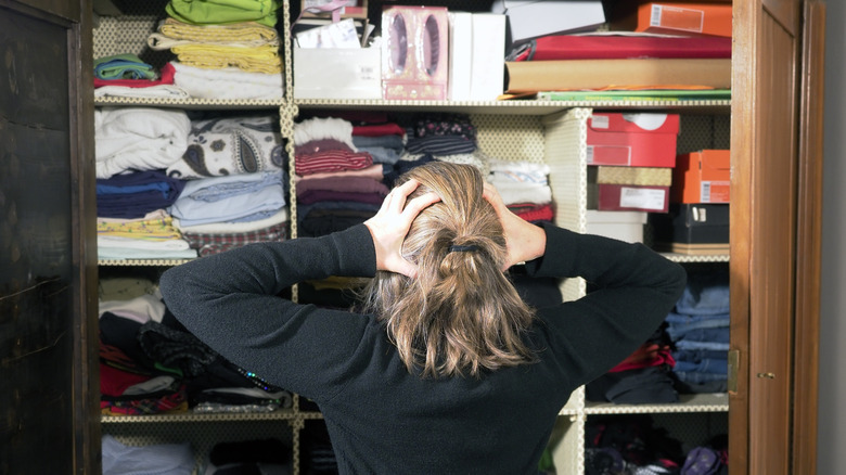 Woman standing in front of a cluttered closet, her hands on her head in frustration