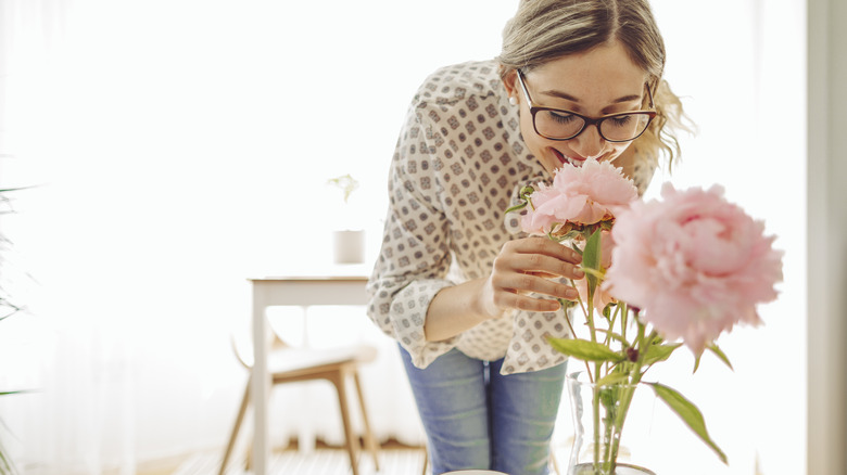 woman smelling peonies in vase