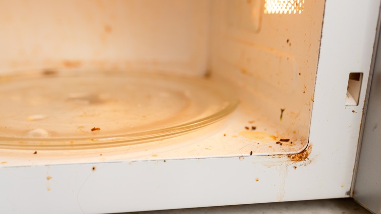 A dirty microwave stands with its door open.