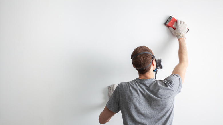 man using sandpaper on wall