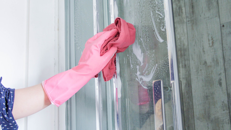 lady wiping shower door with rubber gloves and a cloth