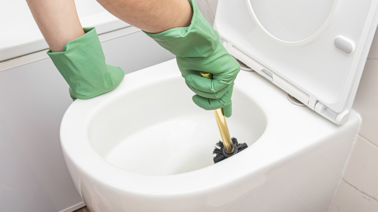 A person wearing green gloves cleans the inside of a toilet bowl