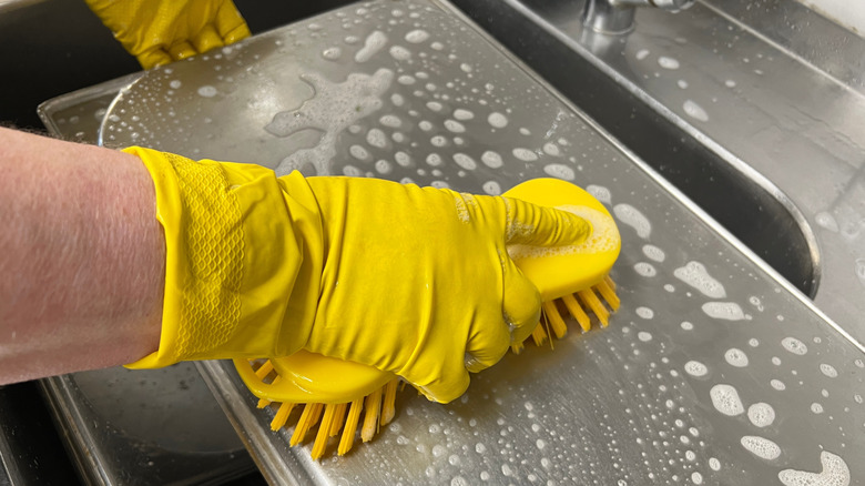 Person washing baking sheet with soapy water and brush.