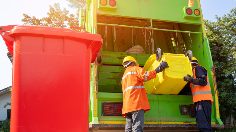 People loading trash into garbage truck