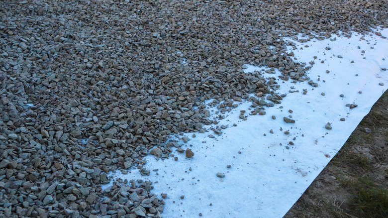 Angular gravel being spread over a white landscape fabric layer