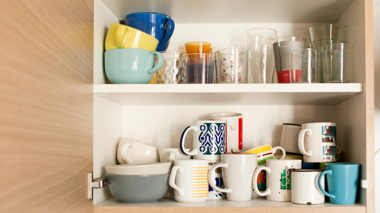 A cabinet filled with a jumble of mugs, cups and glasses