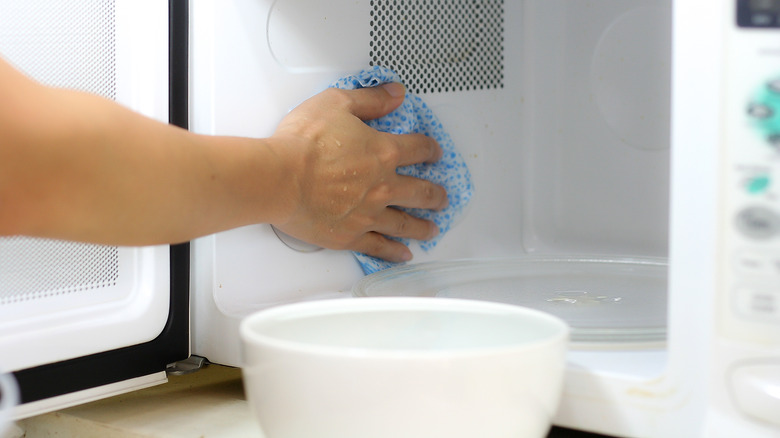 person wiping microwave with rag