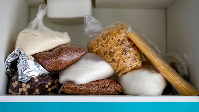 A variety of cereals, flours, and pastas are disorganized on a pantry shelf