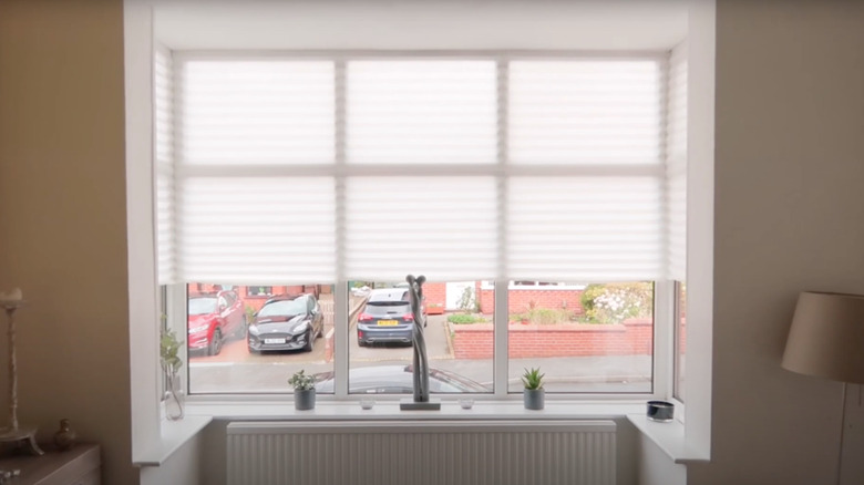 White IKEA SCHOTTIS shades in a bay window overlooking a parking lot.