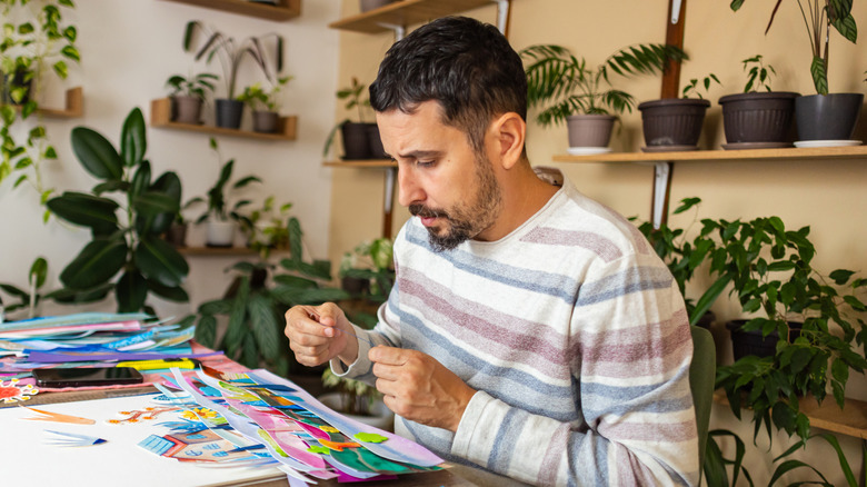 A man making crafts on a table surrounded by plants.
