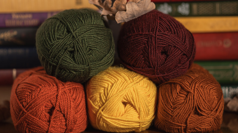 Five skeins of yarn in different autumnal colors with a leaf on top and books in the background
