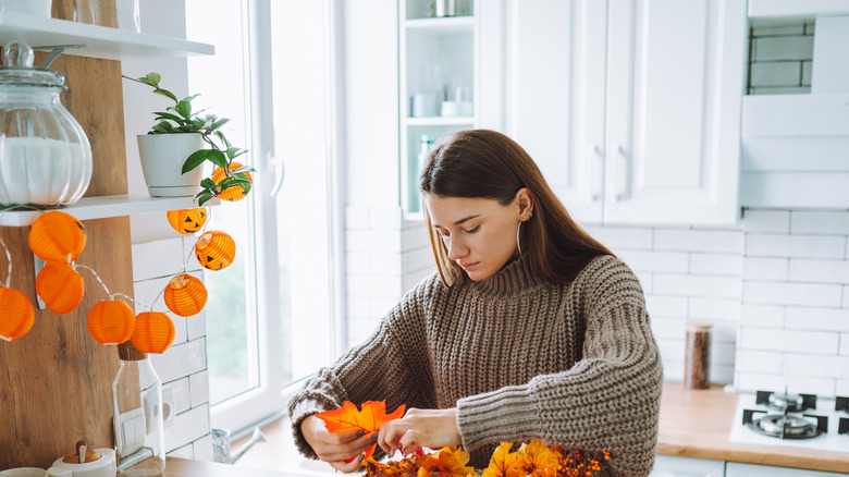 A woman works on a fall DIY decor craft involving leaves